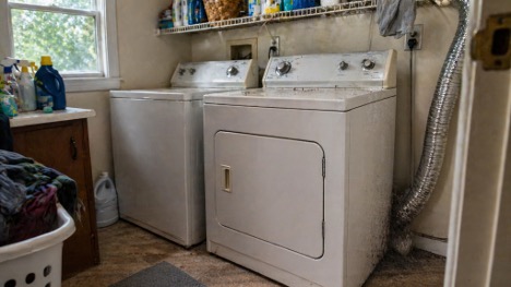 Laundry room in an older home with a dryer and visible lint buildup near the vent, showing a common maintenance issue